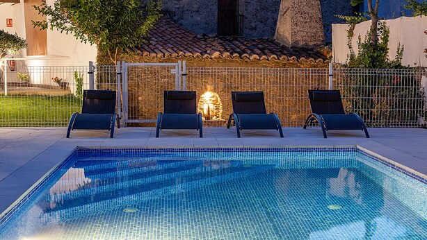 Una piscina con bordes azulejados, rodeada por una valla y cuatro sillas de descanso.