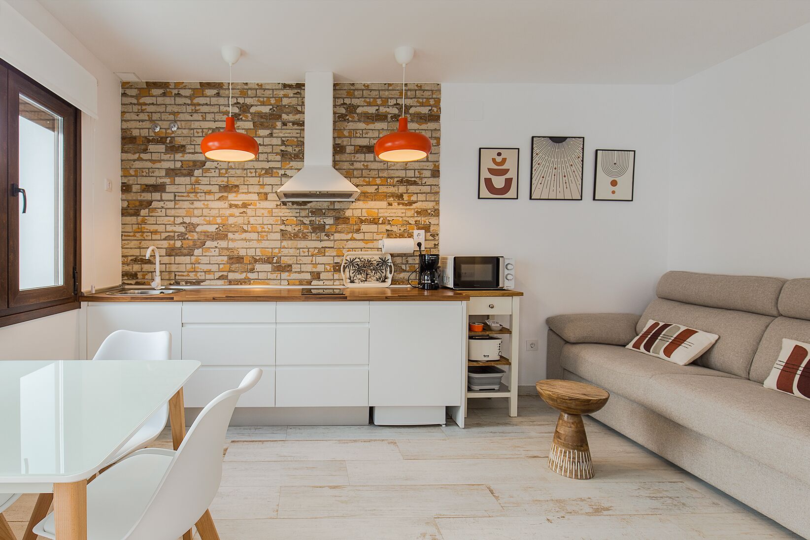 Een moderne keuken met een tegelachtergrond van baksteen, witte kasten, en een eethoek met een witte tafel en stoelen.