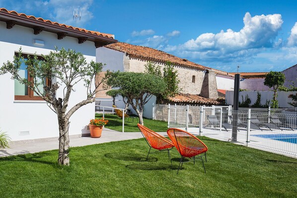 Un patio con piscina, sillas naranjas y una cerca blanca.