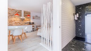 Una cocina moderna con revestimiento de ladrillo, armarios blancos y un comedor con mesa y sillas blancas.