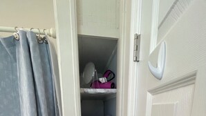 Une salle de bain avec un rideau de douche, un miroir et une étagère où sont pliées des serviettes.