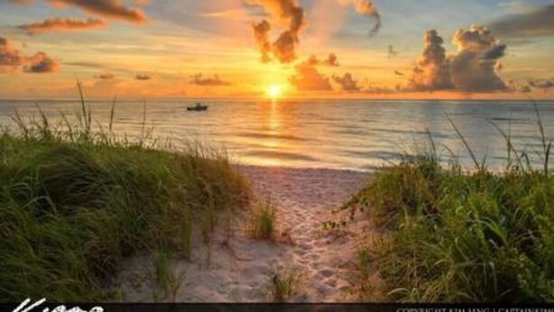 Une scène de plage avec un bateau sur l’eau et un coucher de soleil en arrière-plan.