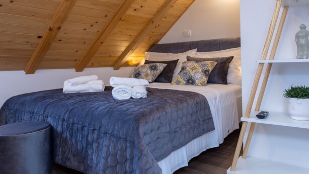 Un dormitorio con techo de madera, una cama con colcha azul oscuro y una mesita de noche blanca con una planta en maceta.