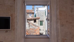 Un ventanal estrecho con vista a un edificio de piedra con tejas de terracota y contraventanas verdes.