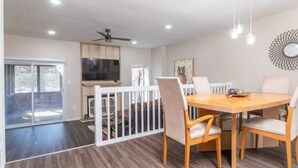A dining area with a wooden table and chairs, a ceiling fan, recessed lighting, and a television.