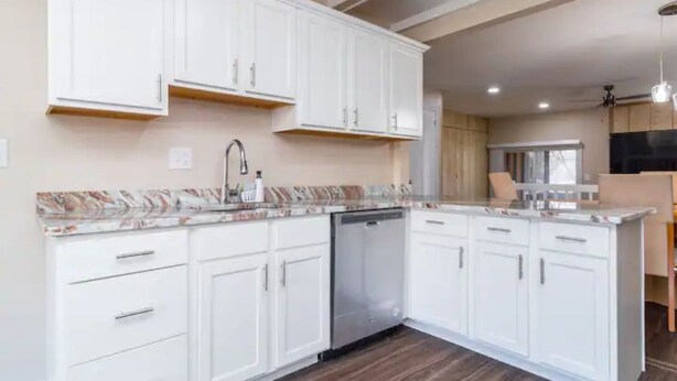 A modern kitchen with white cabinets, a dishwasher, and a marble countertop.