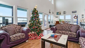 Uma sala de estar espaçosa com uma janela grande, um pinheiro de Natal e dois sofás estampados.