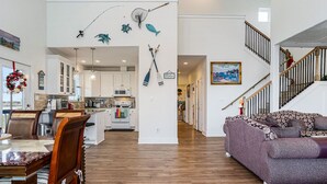Uma sala ampla com mesa e cadeiras de jantar, um sofá roxo e uma cozinha ao fundo.