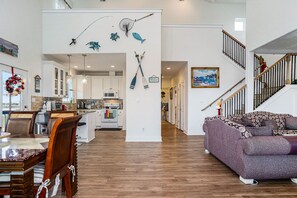 A spacious living area with a dining table and chairs, a purple sofa, and a kitchen in the background.