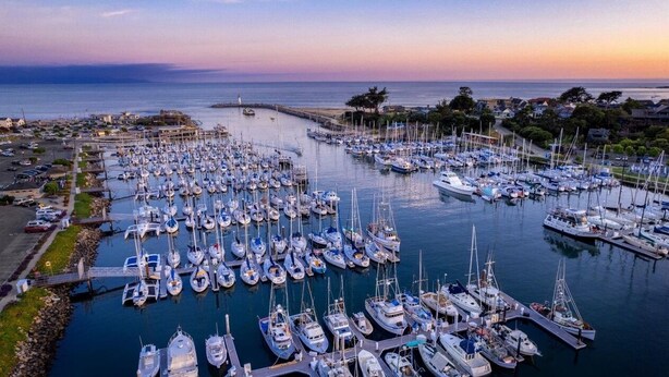 Ein Yachthafen mit zahlreichen vertäuten Booten, einer Pier und Blick auf das Meer und das entfernte Ufer.