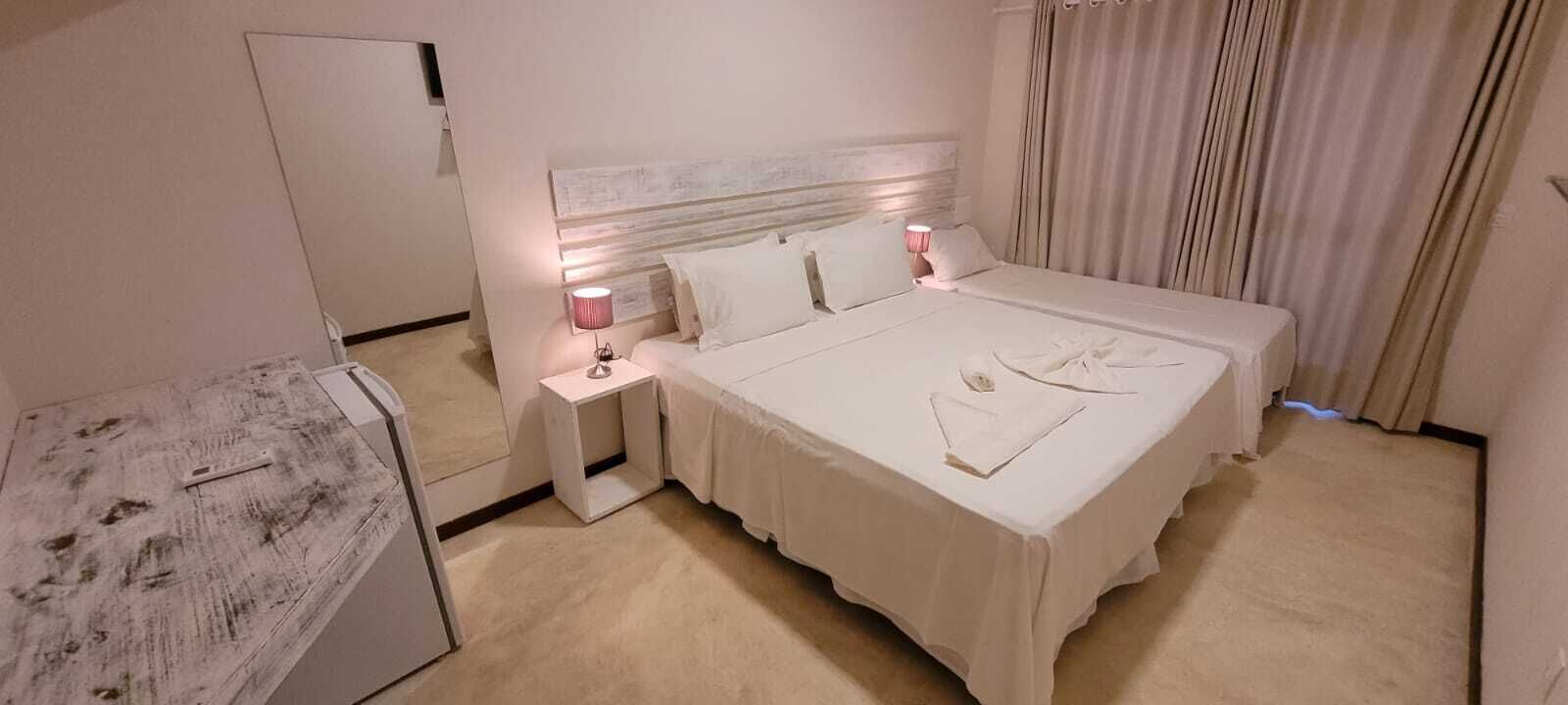Una habitación de hotel con una cama grande, una mesita de noche con lámpara, un espejo y un armario.