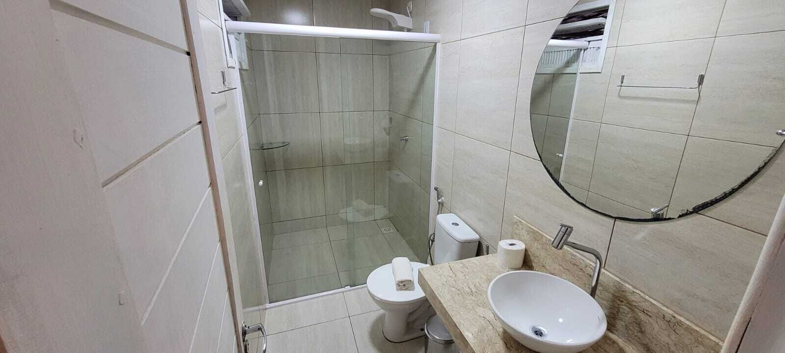 A bathroom with a glass-enclosed shower, a toilet, and a sink with a mirror above it.