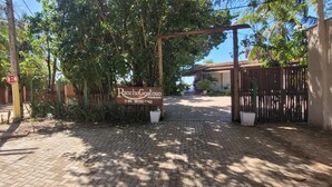 Une entrée fermée par un portail, agrémentée d’une enseigne indiquant « RanchoGostoso », un chemin pavé et une clôture en bois.