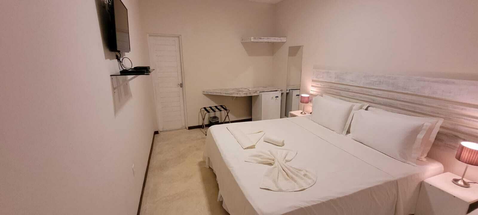 Une chambre d’hôtel avec un lit, un téléviseur fixé au mur, une petite table avec une lampe et une porte.