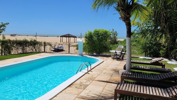 Une piscine avec vue sur la plage, un kiosque et des chaises longues.