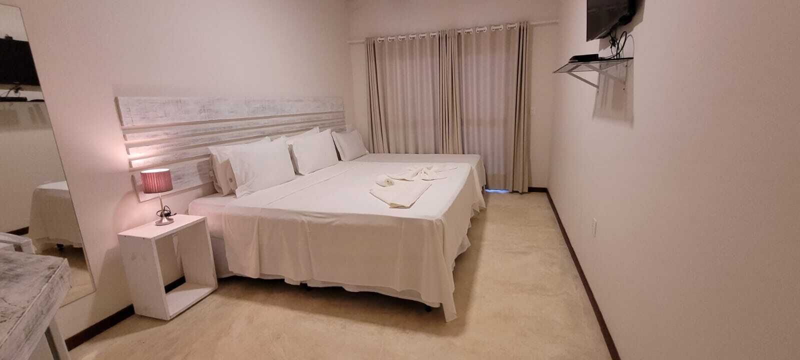 A bedroom with a bed, bedside table, lamp, and curtains.