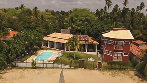 Une propriété située en bord de mer, dotée d’une piscine, d’un voilier et d’un bâtiment rouge avec de nombreuses fenêtres.