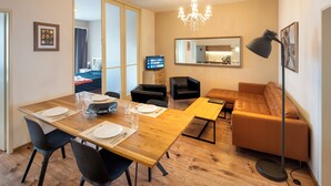 A modern living room with a wooden dining table, black chairs, a brown leather sofa, and a large mirror. - NEW TOWN - 5 ROOM 3 BALCONY APPLE (Hlavní mesto Praha)