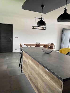 A modern kitchen with a dark countertop, wooden accents, and pendant lighting.