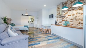 Una sala de estar moderna con un sofá, un comedor con sillas y una cocina con salpicadero de ladrillo y luces colgantes.