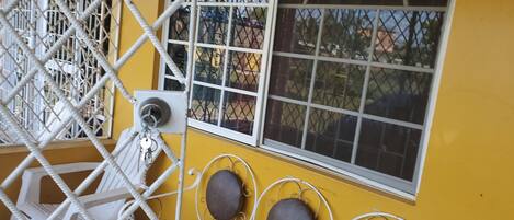 Un mur jaune avec une fenêtre, une porte en métal et un banc.