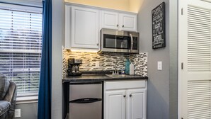 Una cocina compacta con armarios blancos, un refrigerador de acero inoxidable, un microondas y un salpicadero de azulejos.
