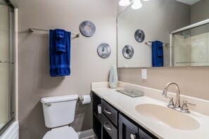 Une salle de bain avec des toilettes, un lavabo et un miroir. Des serviettes bleues sont suspendues sur un porte-serviettes.