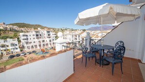Ein Balkon mit Tisch und Stühlen, der auf ein Wohngebiet mit bunten Gebäuden und einem Spielplatz Blick bietet.