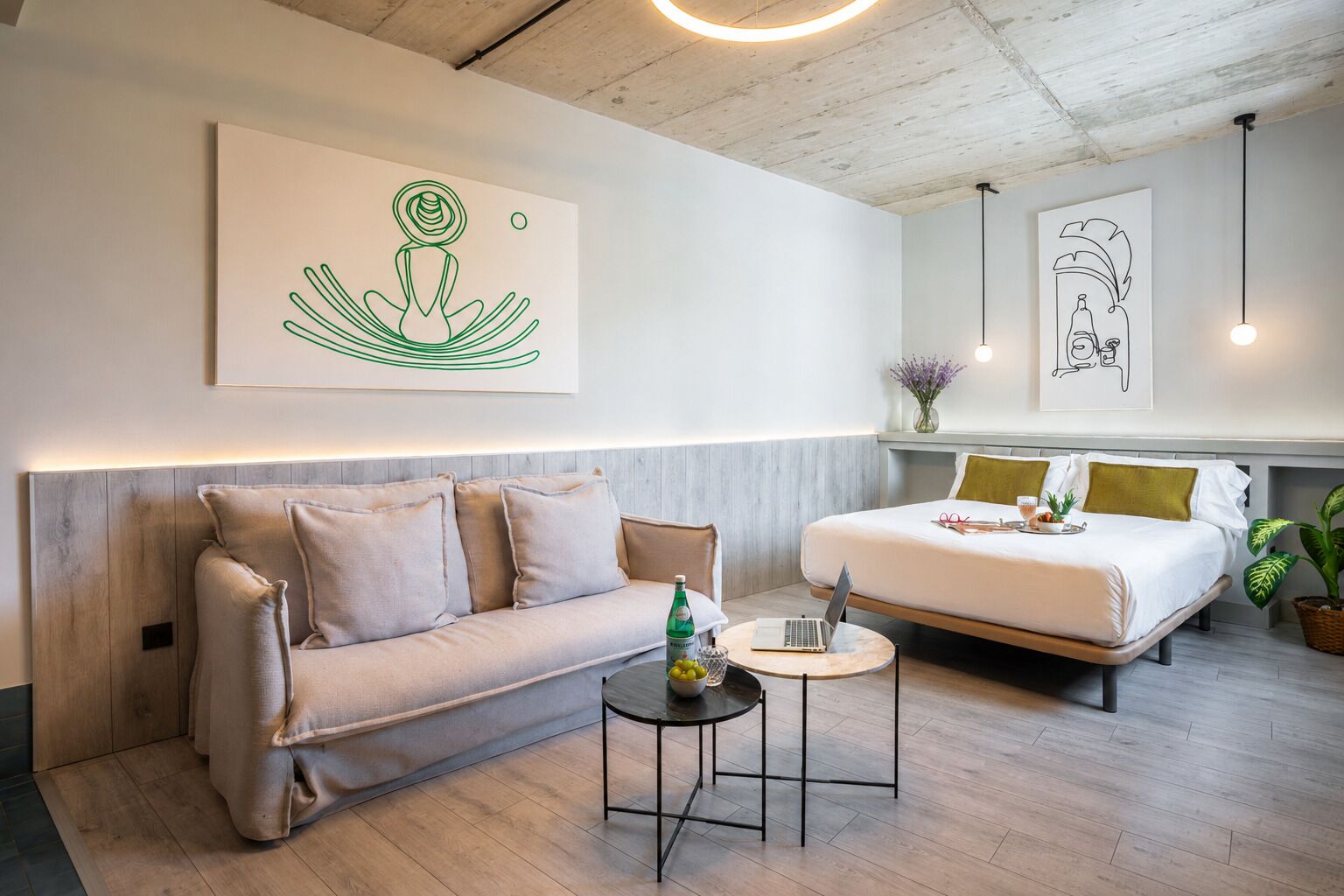 A modern hotel room with a sofa, a small round table, a bed, and artwork on the walls.