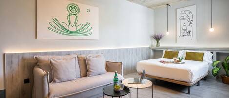 A modern hotel room with a sofa, a small round table, a bed, and artwork on the walls.