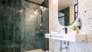 Un baño moderno con ducha de vidrio, lavabo blanco y salpicadero decorativo.