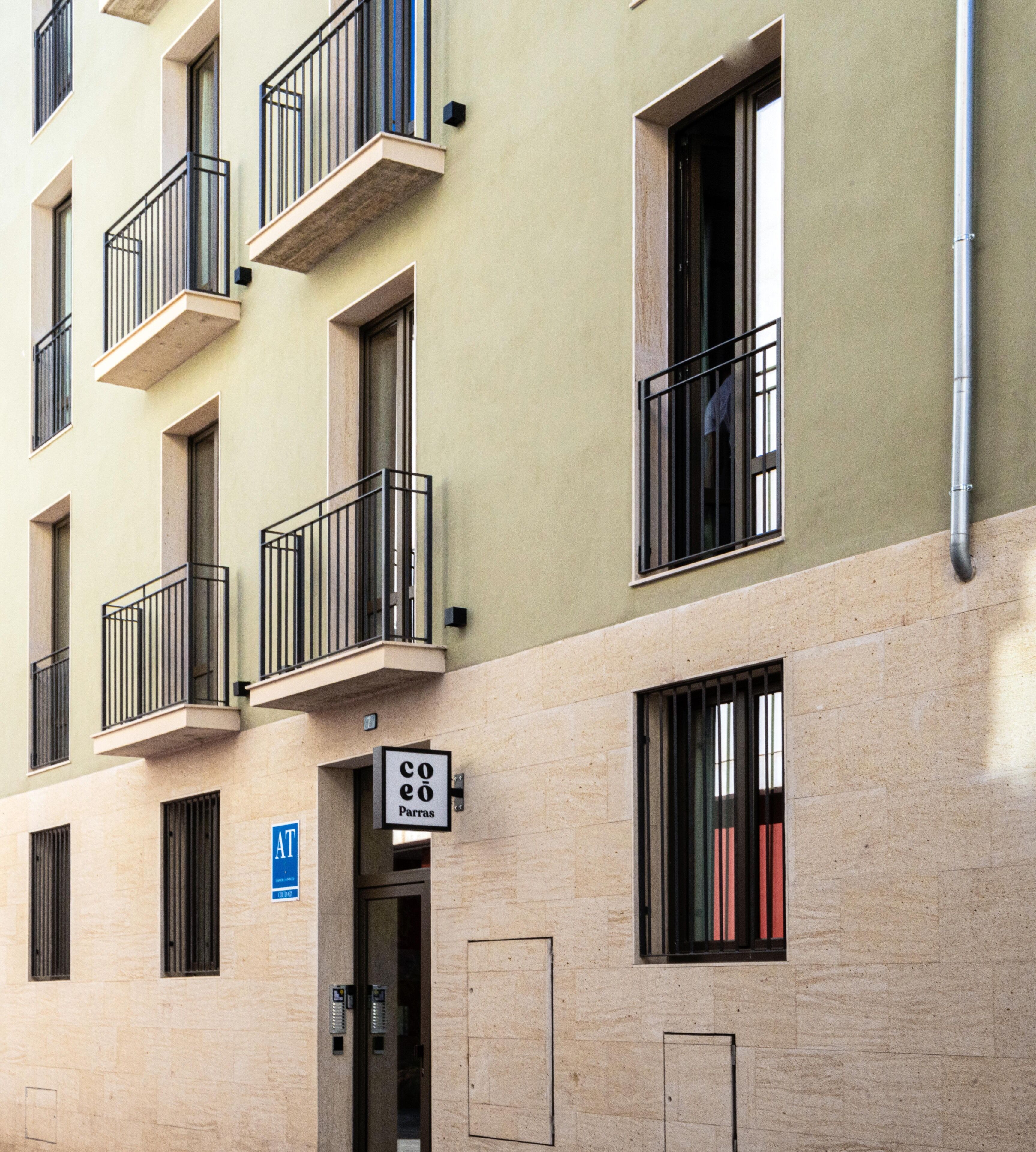 Un edificio de varios pisos con balcones, una entrada visible y un letrero que indica una cafetería.
