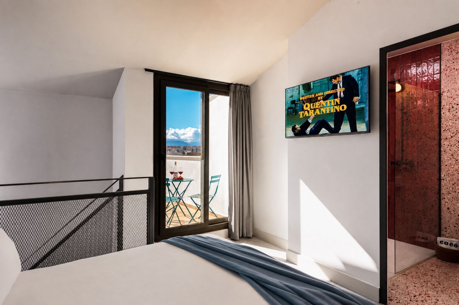 Een hotelkamer met een bed, een balkon met een tafel en stoelen, en een poster aan de muur.