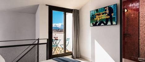 A hotel room with a bed, a balcony with a table and chairs, and a poster on the wall.