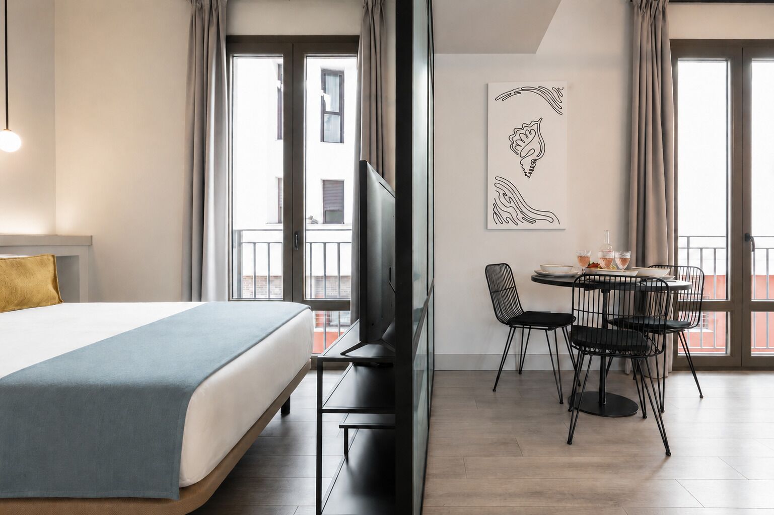 A hotel room with a bed, a TV, a dining area with chairs and a table, and a balcony with curtains.