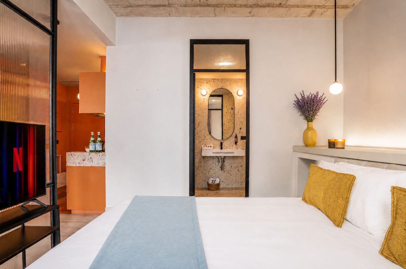 Habitación de hotel con cama, mesita de noche, espejo, lavabo y televisor.
