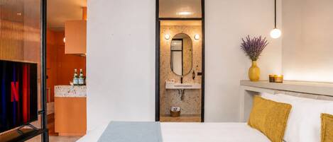 Une chambre d’hôtel avec un lit, une table de chevet, un miroir, un lavabo et une télévision.