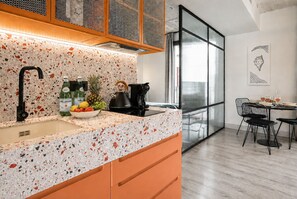 A modern kitchen with a speckled countertop, a kettle, and a bowl of fruit. - Coeo Parras Design Apartments (Málaga)