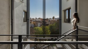 Vista a través de una ventana con reja metálica, que muestra un paisaje urbano con edificios y zonas verdes.