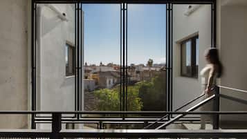 Vista a través de una ventana con reja metálica, que muestra un paisaje urbano con edificios y zonas verdes.