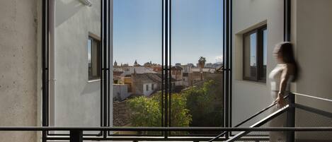 Vista attraverso una finestra con inferriata, su un paesaggio urbano con edifici e vegetazione.