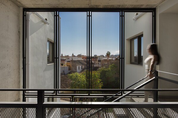A view through a window with a metal grid, overlooking a cityscape with buildings and greenery.