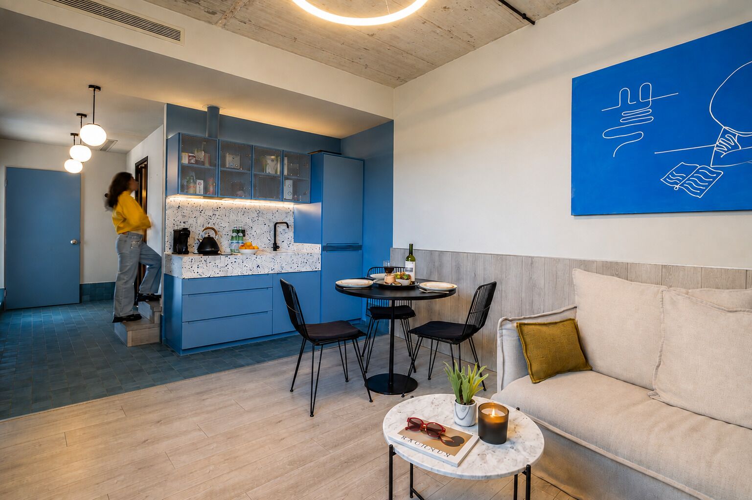 Una sala moderna con un sofá, una mesa de centro con un libro y vasos, y un comedor con una mesa y sillas.
