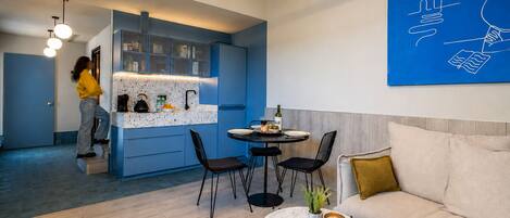 Una sala moderna con un sofá, una mesa de centro con un libro y vasos, y un comedor con una mesa y sillas.