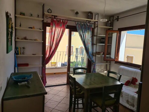 A dining area with a table and chairs, a blue basin on a counter, and a balcony with a railing.