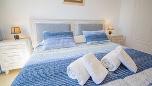 A neatly made bed with blue bedding, two bedside tables with lamps, and a door in the background. - Marina de la Duquesa 516 (Manilva)