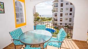 A balcony with a glass table and chairs, a pool, and a view of a building with balconies. - Marina de la Duquesa 516 (Manilva)