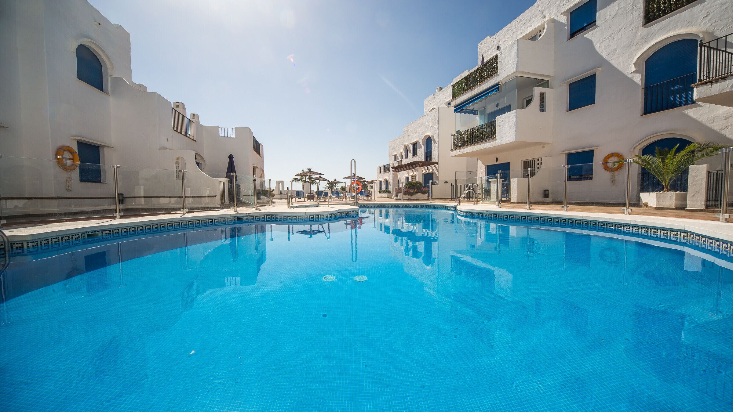 A swimming pool with clear blue water, surrounded by white buildings with balconies and windows.