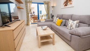 A modern living room with a grey sofa, wooden coffee table, and a TV on a wooden cabinet. - Mikonos Playa apto 15 (Manilva)