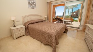 Une chambre à coucher avec un lit, une table de chevet, une lampe et une vue sur l’extérieur grâce à une porte vitrée.